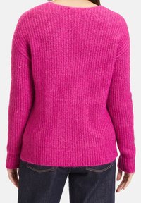 Stickad tröja i klar rosa, med ett strukturerat ribbmönster, rund halsringning och avslappnad passform med långa ärmar och sidslitsar.