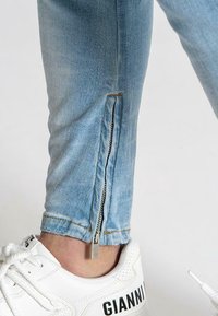 Ljusblå denimjeans med dragkedjedetalj vid vristen, med en silverfärgad dragkedja och synliga sömmar. Bärs med vita sneakers.