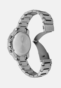 Roostevabast terasest käekell, millel on ketaslakk, ümmargune korpus ja poleeritud hõbedane viimistlus. Omab graveeritud tagust, millel on brändi logo.