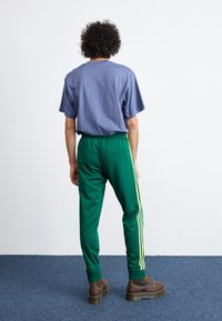 Ljusblå bomulls-t-shirt med korta ärmar, som matchas med gröna sweatpants med gula sidostråk. Bruna snörboots fulländar looken.