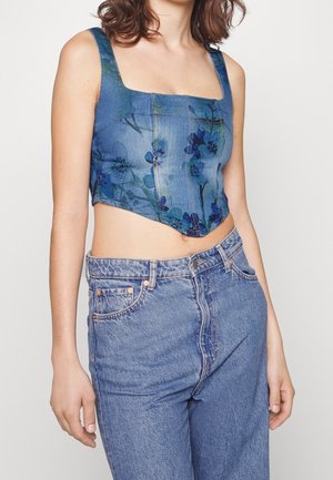 Top en denim avec une encolure carrée, présentant un motif floral bleu et vert. Associé à un jean en denim bleu taille haute.