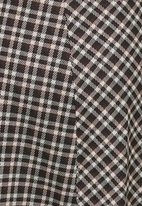 Brun och krämfärgad rutig tyg med ett diagonalt mönster som innehåller olika storlekar av rutor, texturerad yta och en mjuk framtoning.