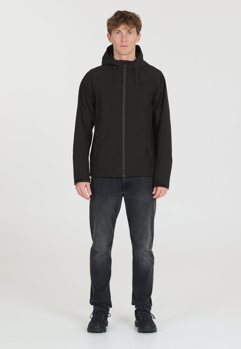 Black hooded jacket with a zip front, elastic cuffs, and side pockets. Worn over dark jeans and black hiking boots. Smooth fabric texture.