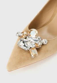 Beige suede pointed-toe shoe with a cluster of large clear and amber faceted gem embellishments on the front.