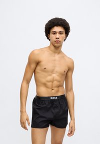 Fekete fürdőnadrág könnyű anyagból, elasztikus derékpánttal, amelyen "BOSS" logó található, és kényelmes, bő szabással.