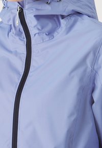 Veste imperméable violet clair avec un col montant, une fermeture éclair noire et une capuche réglable avec cordon. Texture lisse, conçue pour une utilisation en extérieur.