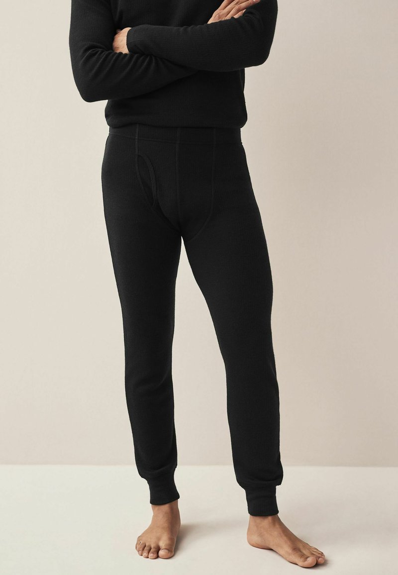 Schwarze thermische Leggings mit gerippter Textur, ausgestattet mit einem elastischen Bund und schmal zulaufenden Bündchen; konzipiert für Wärme und Komfort.
