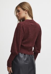 Burgunderroter gestrickter Pullover mit taillierter Passform, gepufften langen Ärmeln und rundem Halsauschnitt. Weiche Textur, gerippte Manschetten und Bund.
