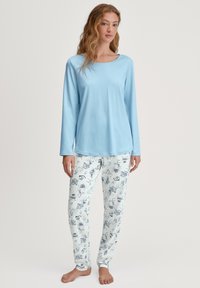 Maglietta azzurra a maniche lunghe con scollatura arrotondata abbinata a pantaloni bianchi caratterizzati da un motivo blu di vari oggetti illustrati.