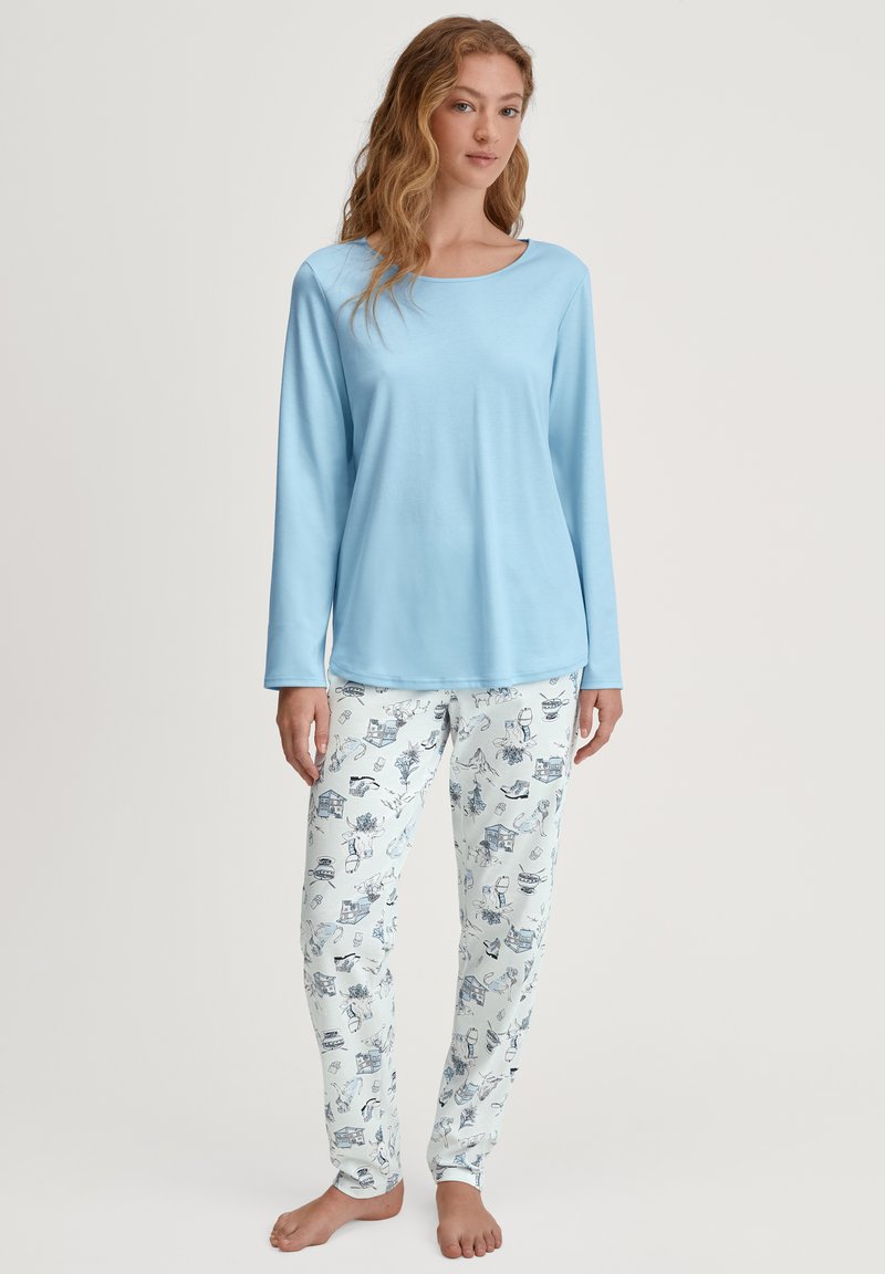 Maglietta azzurra a maniche lunghe con scollatura arrotondata abbinata a pantaloni bianchi caratterizzati da un motivo blu di vari oggetti illustrati.
