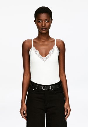 Biały top na ramiączkach z dekoltem w serek i koronkowym wykończeniem przy szyi, w połączeniu z czarnymi, wysokim stanem spodniami i czarnym paskiem.