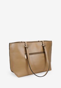 Bolso tote de cuero marrón claro con dos asas superiores, un bolsillo con cremallera en la parte frontal y acentos de costura negra. Textura suave y forma estructurada.