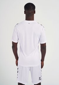 Witte sporttrui met korte mouwen, voorzien van zwarte accenten op de schouders en een logo aan de linkerkant, gemaakt van een gladde stof.