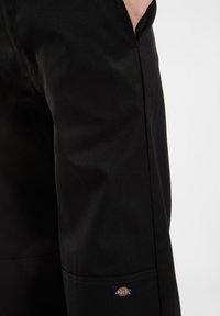 Čierne pracovné nohavice vyrobené z odolnej látky. Majú rovný strih, bočné vrecká a na ľavom boku sa nachádza nášivka s logom Dickies.