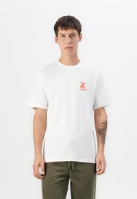 White cotton t-shirt with short sleeves, features a red graphic print with text on the left chest area. Smooth texture and classic fit.