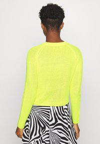 Neonowy żółty sweter z dzianiny z długimi rękawami, lekką fakturą i ściągaczami, w zestawieniu z czarno-białą spódnicą w paski zebry.