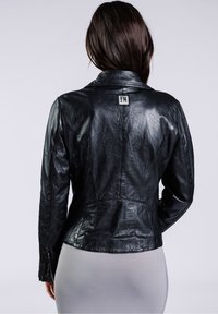 Černá kožená bunda s mírně zmraženou texturou, s klopovým límcem a malou logem na zadní straně. Má zipové manžety.