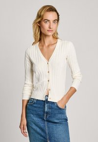 Krémový cardigan s výstrihom do V a rebrovanou textúrou, zapínanie na gombíky a trojštvrťové rukávy, skombinovaný s modrou denimovou sukňou.