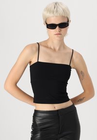 Top corto nero con spalline sottili, design aderente e trama liscia. Abbinato a pantaloni in pelle a vita alta con borchie.
