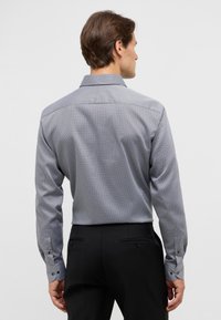 Camicia a maniche lunghe con motivo geometrico, blu e bianco, con colletto a punta, polsini con bottone e una texture liscia.