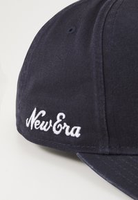 Tumedast sinine kangast müts, millel on kõver visiit. Omab valget tikitud "New Era" logo ja väikest ventilatsiooniava.