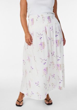 Kvinde iført hvid maxi nederdel med smocket talje og lys lilla blomstermønster, kombineret med sorte flip-flop sandaler.