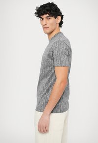 Szara koszulka z nadrukiem logo na całej powierzchni, krótkimi rękawami i okrągłym dekoltem, wykonana z miękkiej tkaniny o gładkiej fakturze.