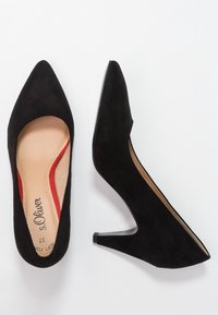 Zapatos de tacón alto de ante negro con punta afilada, que presentan un diseño con recortes y acentos rojos en la plantilla. Acabado suave y texturizado.