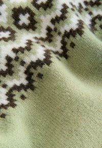 Strickstoff in Hellgrün mit einem gemusterten Design in Dunkelbraun und Weiß. Weiche Textur mit sichtbaren Fasern.