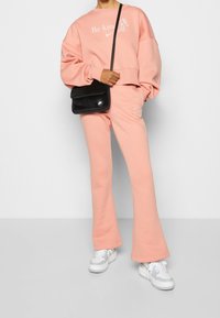 Rosa kortärmad sweatshirt med texten "Var snäll" och matchande utställda sweatpants. Kommer med en svart, mjuk tygaxelväska. Vita sneakers fulländar looken.