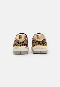 Lekkerprikkede sneakers med gullmetallisk hæl og svart overdel, samt en beige såle, med teksturert stoff og subtile merkevaredetaljer.