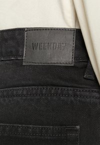 Musta farkut ovat tekstuuripintaiset, ja vyötäröltä löytyy "WEEKDAY"-laidalla kohokuvioitu nahkatagi, joka esittelee puhdasta ja minimalistista muotoilua.