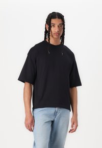 Musthave must-öine t-särk langen õlgadega, valmistatud siledast puuvillast, millele on sobitatud helesinised teksad, et saavutada lõdvestunud välimus.