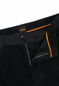 Czarne spodnie sztruksowe z zapięciem na guzik, zamkiem błyskawicznym i pomarańczowymi akcentami na pasku, z wzorzystym wnętrzem. Widoczna metka marki.