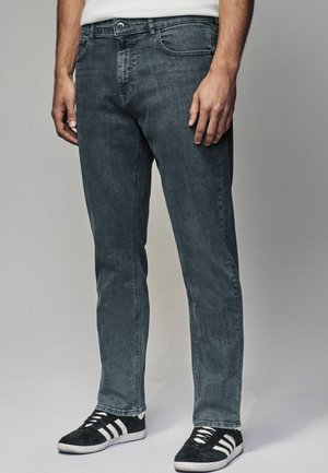Jeans in denim grigio con taglio dritto, cinque tasche, passanti per cintura e una texture sottile. Abbinati a scarpe da ginnastica nere con strisce bianche.