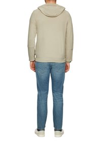 Sweatshirt à capuche gris clair avec une finition texturée, associé à un jean en denim bleu. Le jean a un design classique à cinq poches.