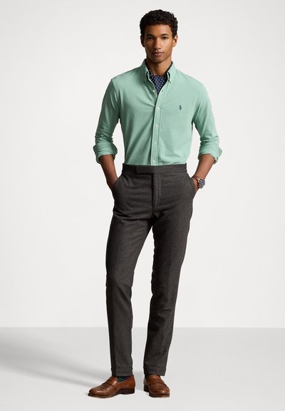 Camisa botões de cor verde-claro, calças em carvão, mocassins castanhos, gravata azul com bolinhas. Tecido suave com um corte ajustado, design sob medida.