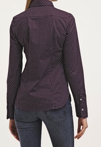 Chemise mauve à boutons avec des pois blancs, dotée d'un col classique et de manches longues, fabriquée en tissu lisse.