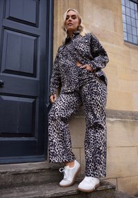 Camisa de estampado de leopardo y pantalones a juego en tejido suave, con un corte holgado y mangas largas, combinados con zapatillas blancas.