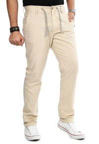 Beige Baumwollmischungshose mit geradem Schnitt, elastischem Bund und einer schwarz-weißen Kordel, sowie seitlichen Taschen. Kombiniert mit weißen Sneakern.