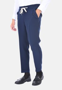 Pantaloni blu navy con vita regolabile, tasche laterali e design affusolato. Indossati con scarpe nere e calzini scuri.