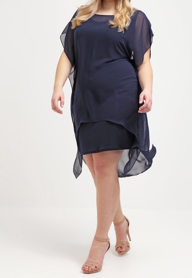 Robe transparente bleu marine avec un col rond, des manches courtes et un ourlet asymétrique. Associée à des sandales à talons à lanières nude.