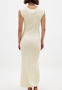 Langes, eng anliegendes cremefarbenes Kleid mit gerippter Textur. Mit kurzen Ärmeln und einem runden Ausschnitt, der bis zu den Knöcheln reicht. Einfacher, einfarbiger Look ohne Muster.