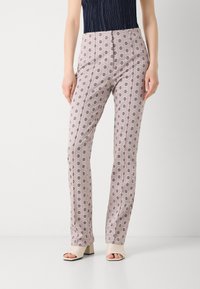Patroonbroeken van lichtroze stof, met cirkelvormige bloemenmotieven, op maat gemaakt en met zijnaad. Gepaard met beige sandalen met blokhak.