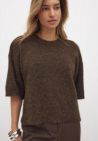 Brauner, strukturierter Strickpullover mit Rundhalsausschnitt und kurzen Ärmeln; hat eine lockere Passform und einen gerippten Saum.