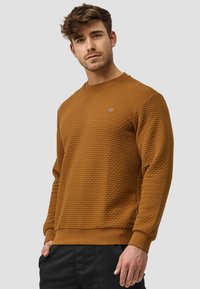 Brauner strukturierter Pullover mit Rundhalsausschnitt, gerippten Manschetten und Bund, mit einem kleinen Logo-Detail auf der Brust.
