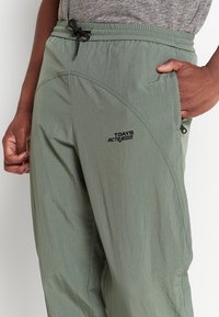 Lekkie, oliwkowozielone spodnie z elastycznym pasem, bocznymi kieszeniami i logo nadrukowanym na udzie. Gładka tekstura, zwężany krój.