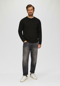 Schwarzer, gesprenkelter Strickpullover mit Rundhalsausschnitt, kombiniert mit hellgrauen Jeans und weißen Turnschuhen. Einfaches Design, lässige Passform.
