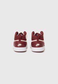 Červené a biele vysoké tenisky Nike pohľad zospodu, s bielym logom a štruktúrovanou pätou pre podporu.