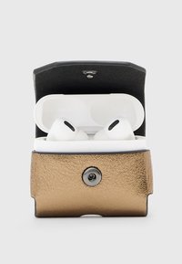 Białe bezprzewodowe słuchawki w otwartej białej ładowarce umieszczone w metalicznej brązowej skórzanej osłonie z zapięciem na zatrzask.